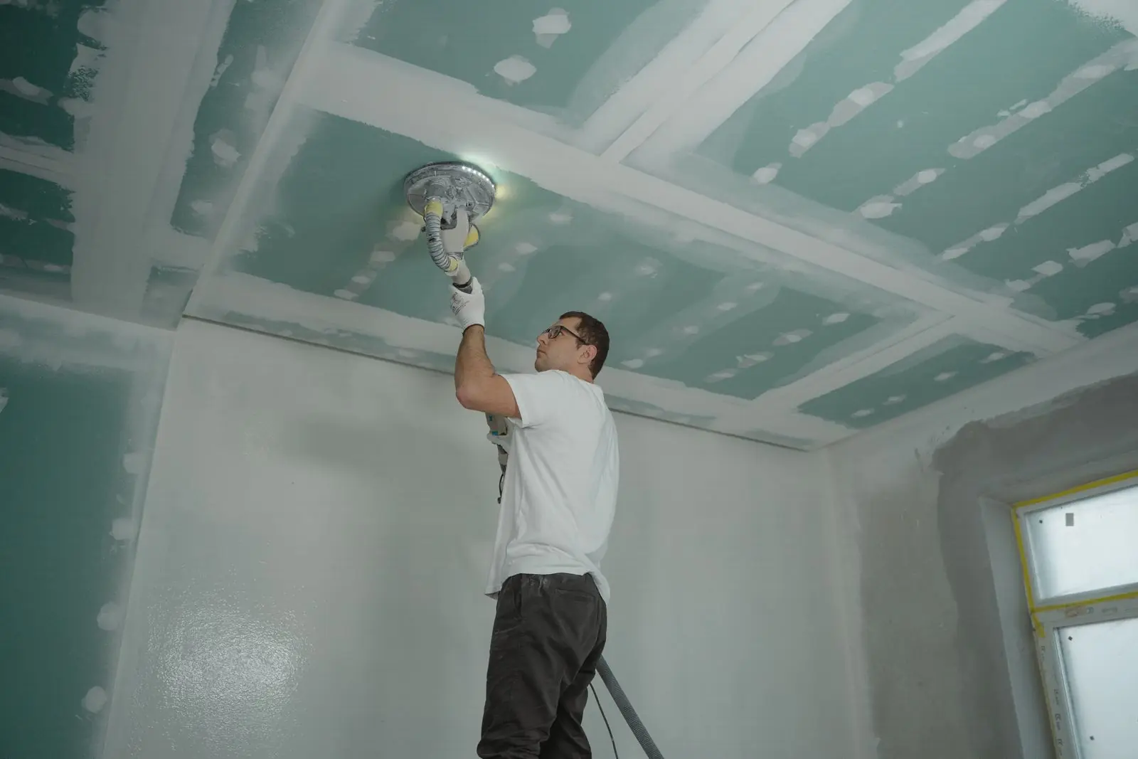 Contractor sanding and refinishing a ceiling during restoration